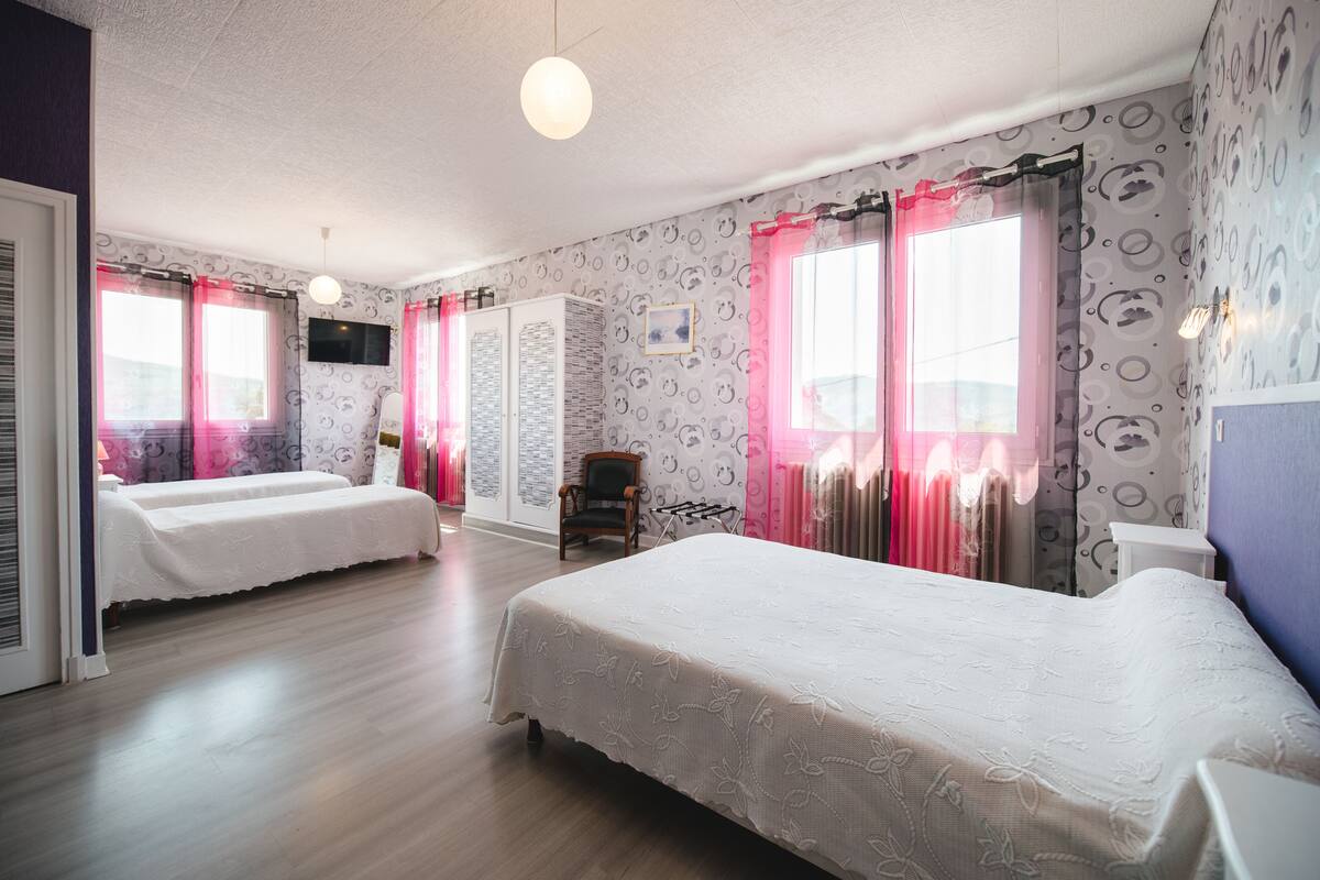 A hotel room with two beds, a chair, a TV, and patterned wallpaper.