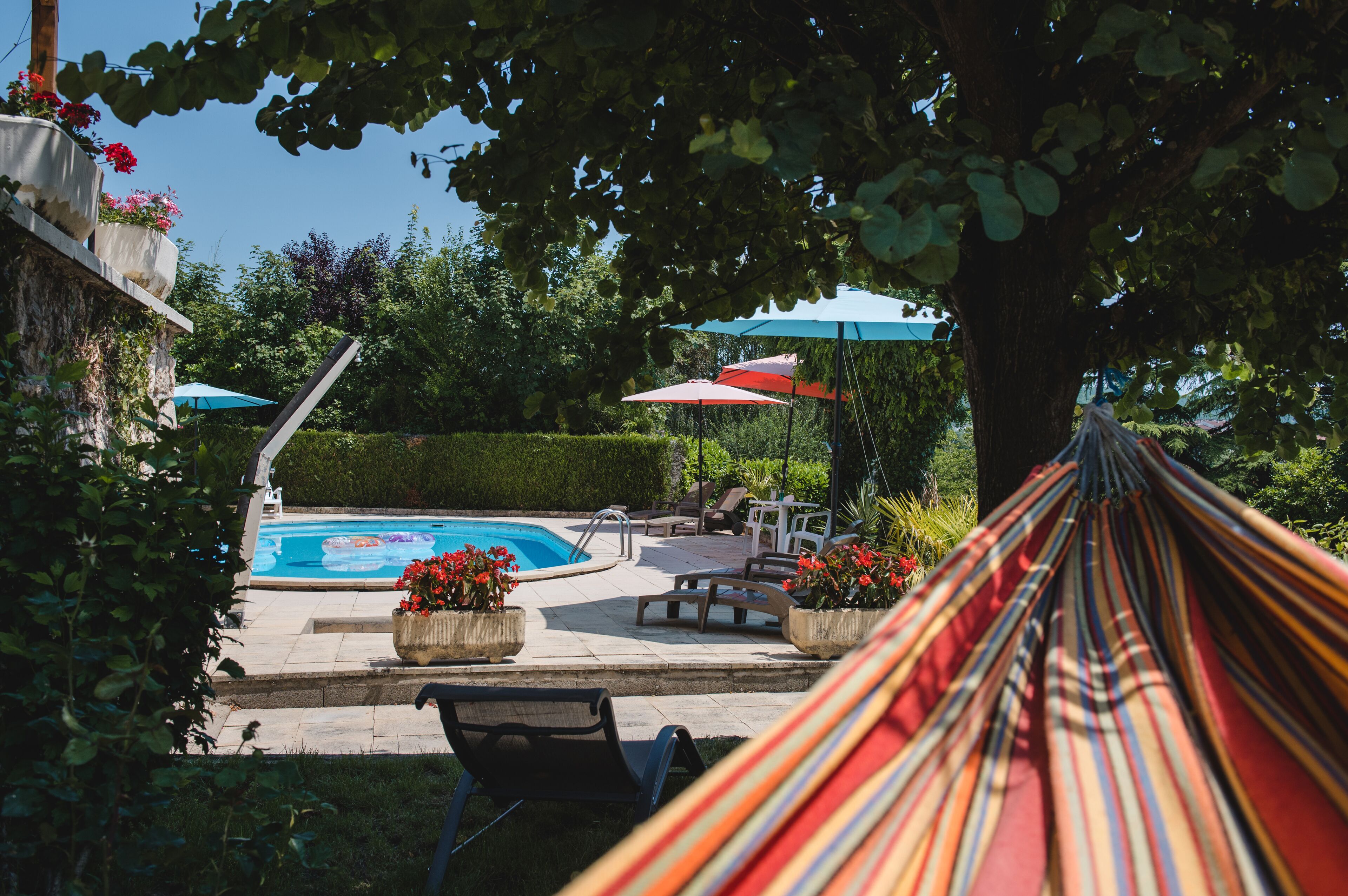 Un área de piscina con una hamaca, sillas de descanso y sombrillas.