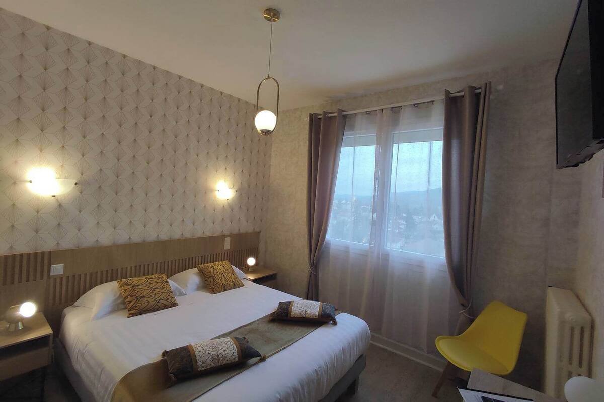 A hotel room with a large bed, two bedside tables with lamps, a window with curtains, and a flat-screen TV mounted on the wall.