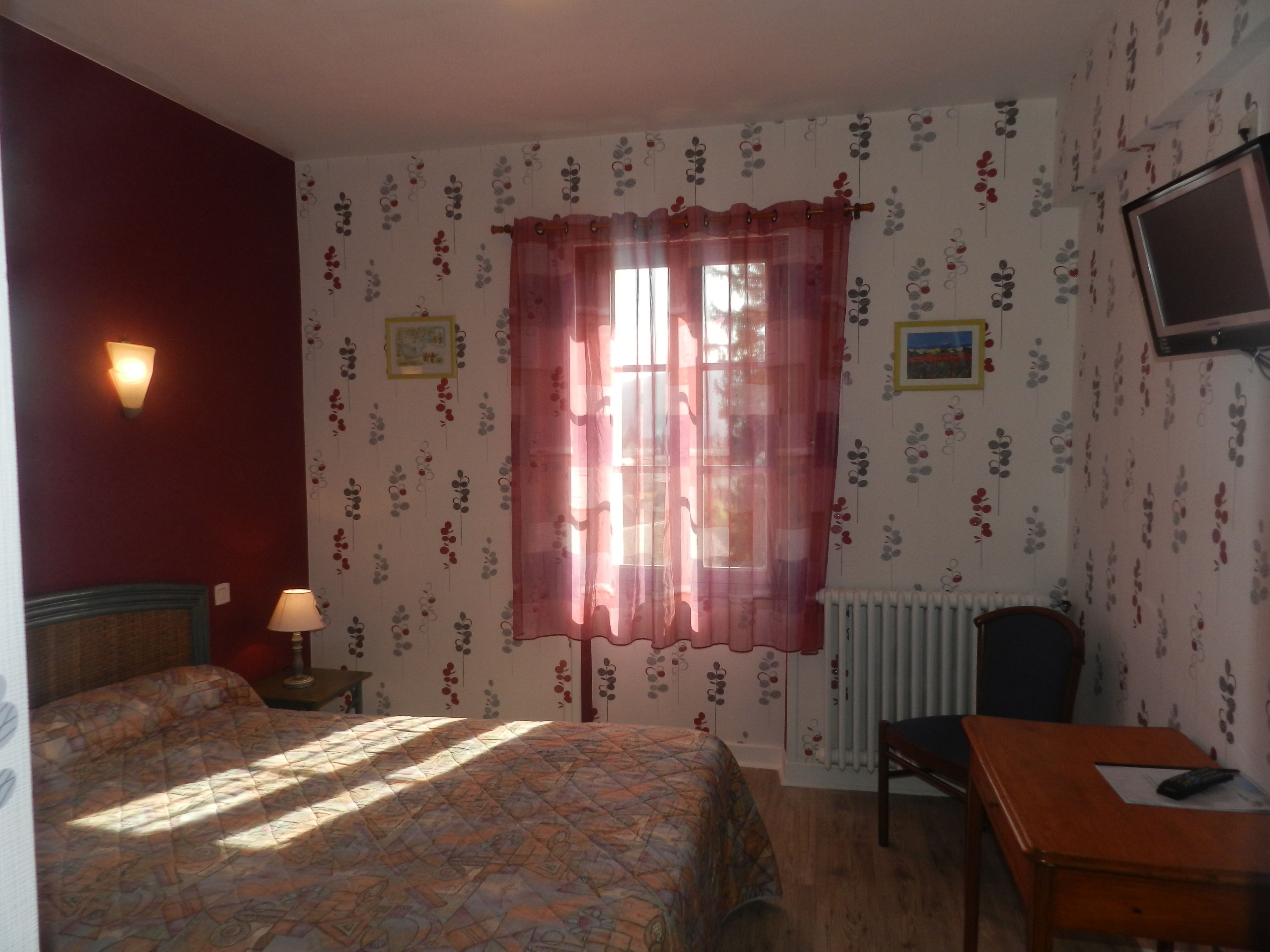 A hotel room with a bed, a desk, a chair, a lamp, a television, and a window with a curtain.