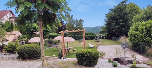 A garden with a wooden pergola, picnic tables, and thatched umbrellas.