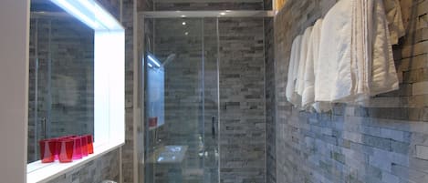 Un baño moderno con cabina de ducha de vidrio, un lavabo blanco y un espejo con marco iluminado.