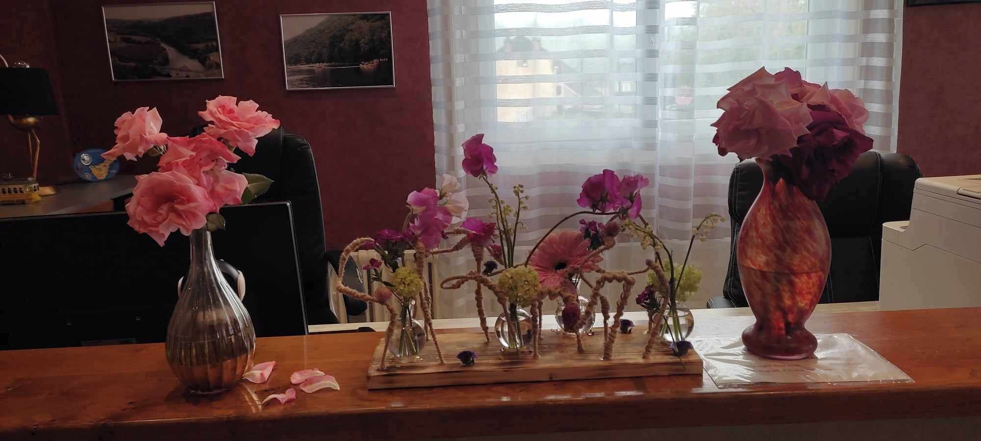 A wooden desk with multiple vases containing flowers.