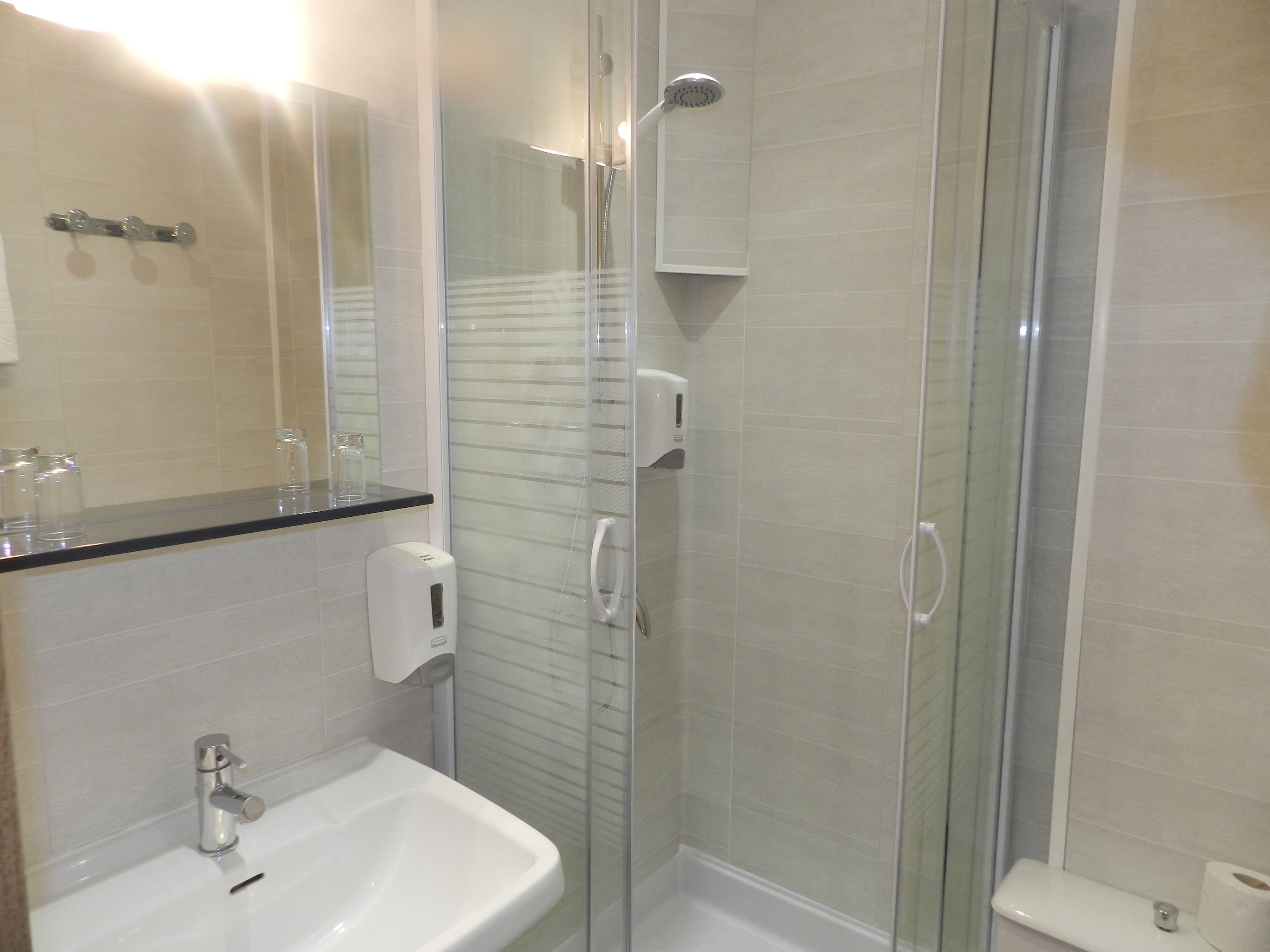 Een moderne badkamer met een douchekabinet van glas, een witte wastafel en een spiegel boven de wastafel.