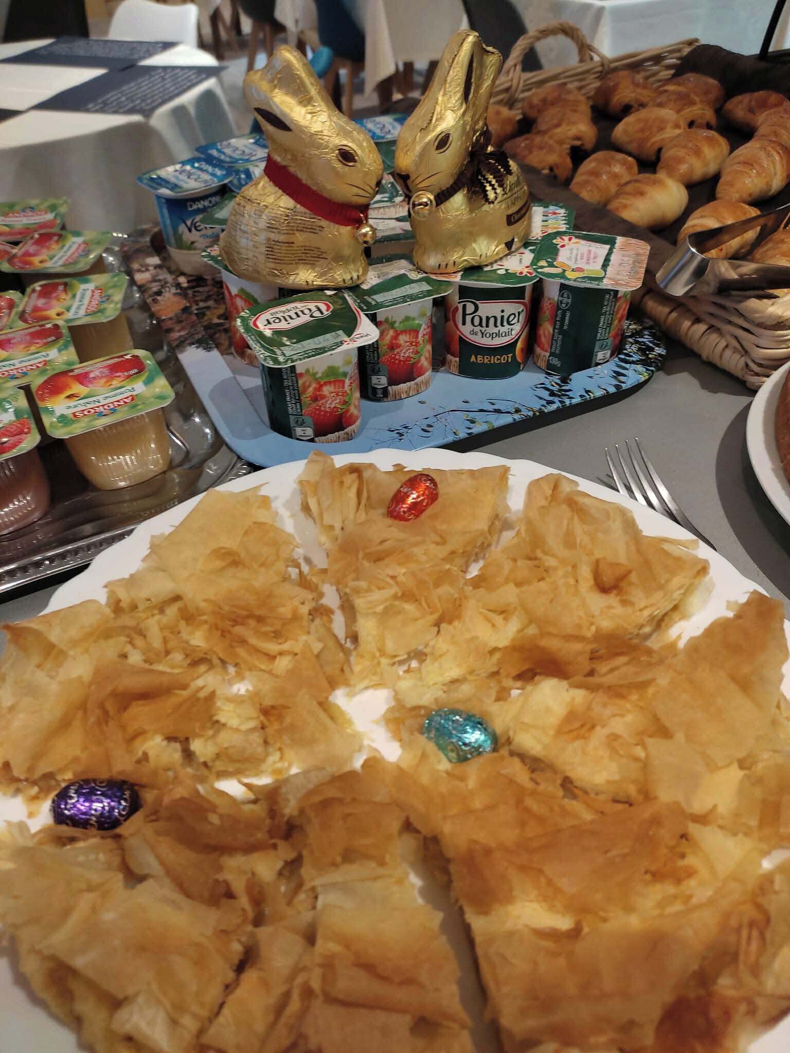 Une table où l’on trouve une variété d’aliments, notamment des pâtisseries, une assiette de baklava et des pots de yaourt.