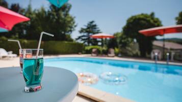 Vista clara de una piscina con un vaso de líquido azul y una pajita, rodeado de sombrillas y sillas de descanso.