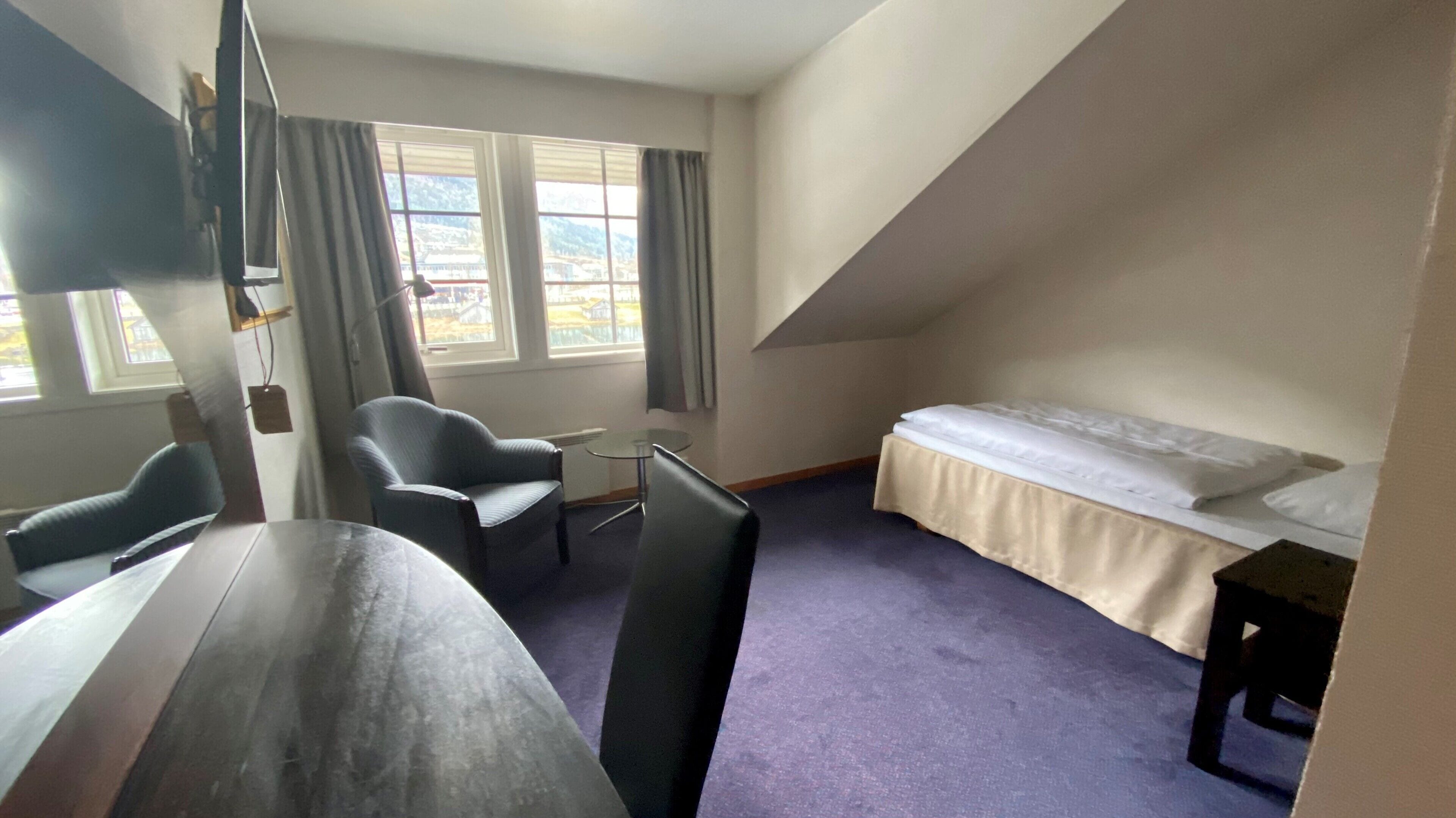 A room with a bed, a desk, a chair, and a window with curtains.