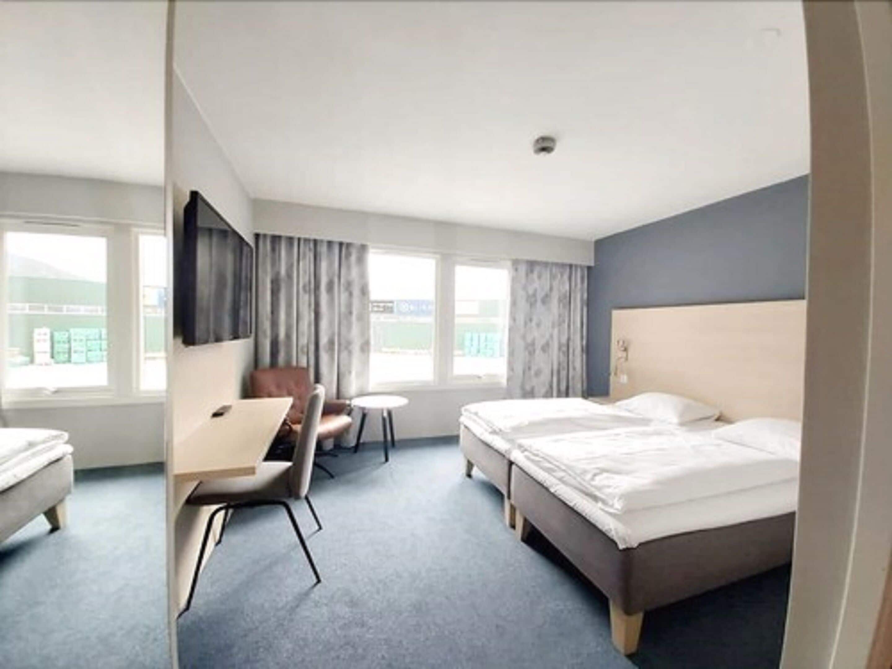 Una habitación de hotel con una cama, un escritorio, una silla y un televisor montado en la pared.