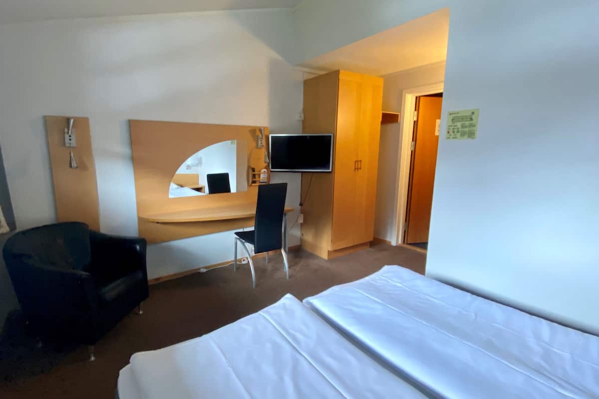A hotel room with a bed, a desk, a chair, a TV, and a mirror.
