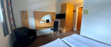 A hotel room with a bed, a desk, a chair, a TV, and a mirror.