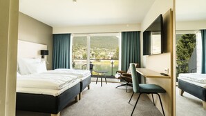 Habitación de hotel con dos camas, un escritorio, una silla y vistas a un lago y montañas.