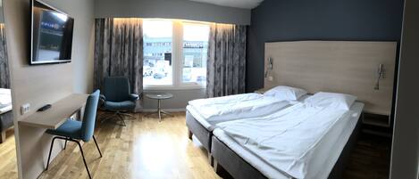 Een hotelkamer met een bed, een bureau, een stoel, een bijzettafeltje en een aan de muur bevestigde televisie.