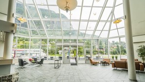 Un vestíbulo amplio con techo de cristal, mobiliario moderno y vistas a un paisaje montañoso.