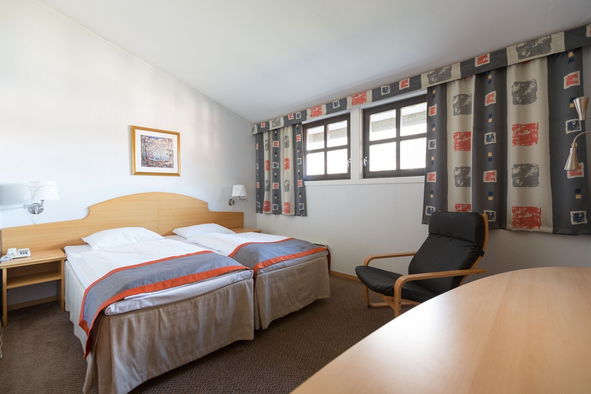 Habitación de hotel con dos camas, un escritorio, una silla, una ventana con cortinas y un cuadro en la pared.