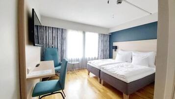 Habitación de hotel con cama, escritorio, silla y televisión montada en la pared.
