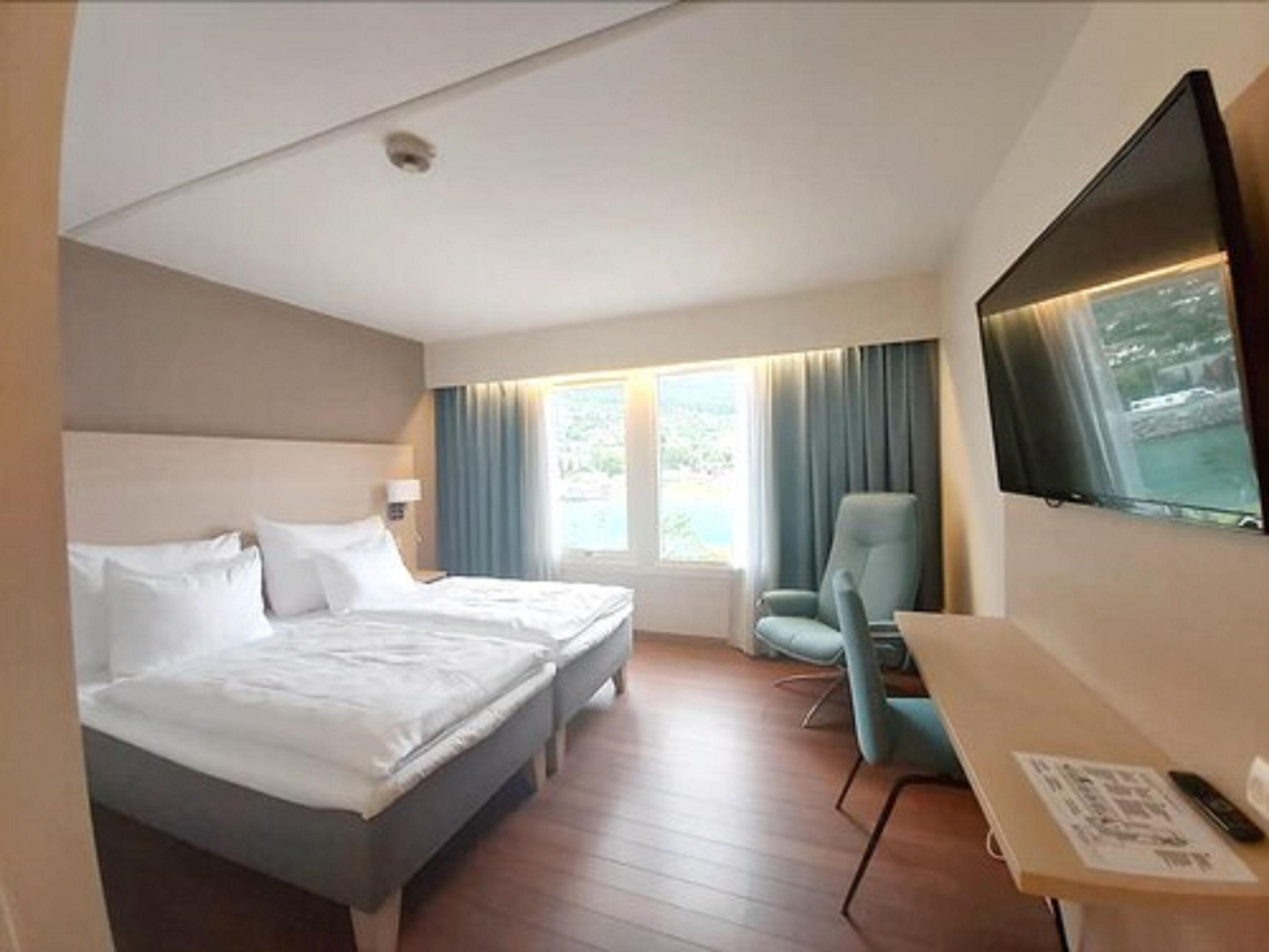 Habitación de hotel con cama, escritorio, silla, televisor y ventana con cortinas.