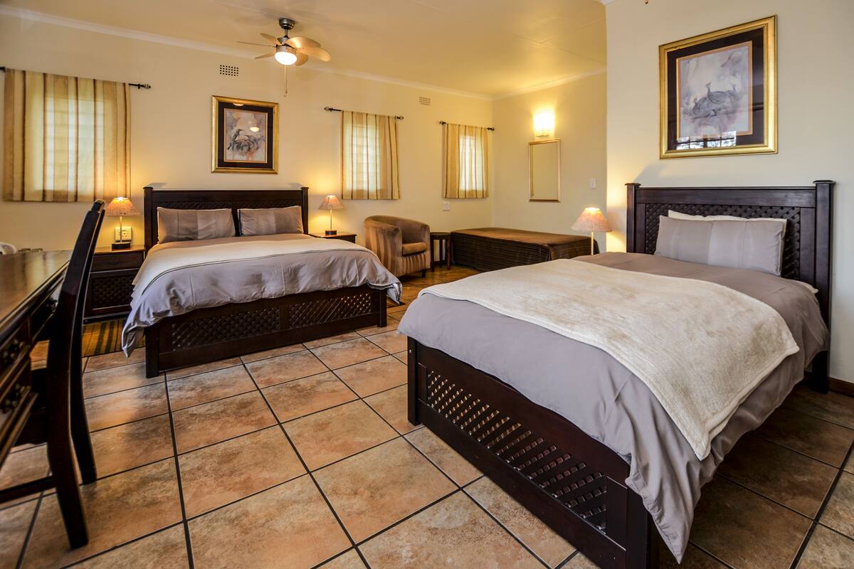 A hotel room with two beds, a desk, a chair, and a ceiling fan.