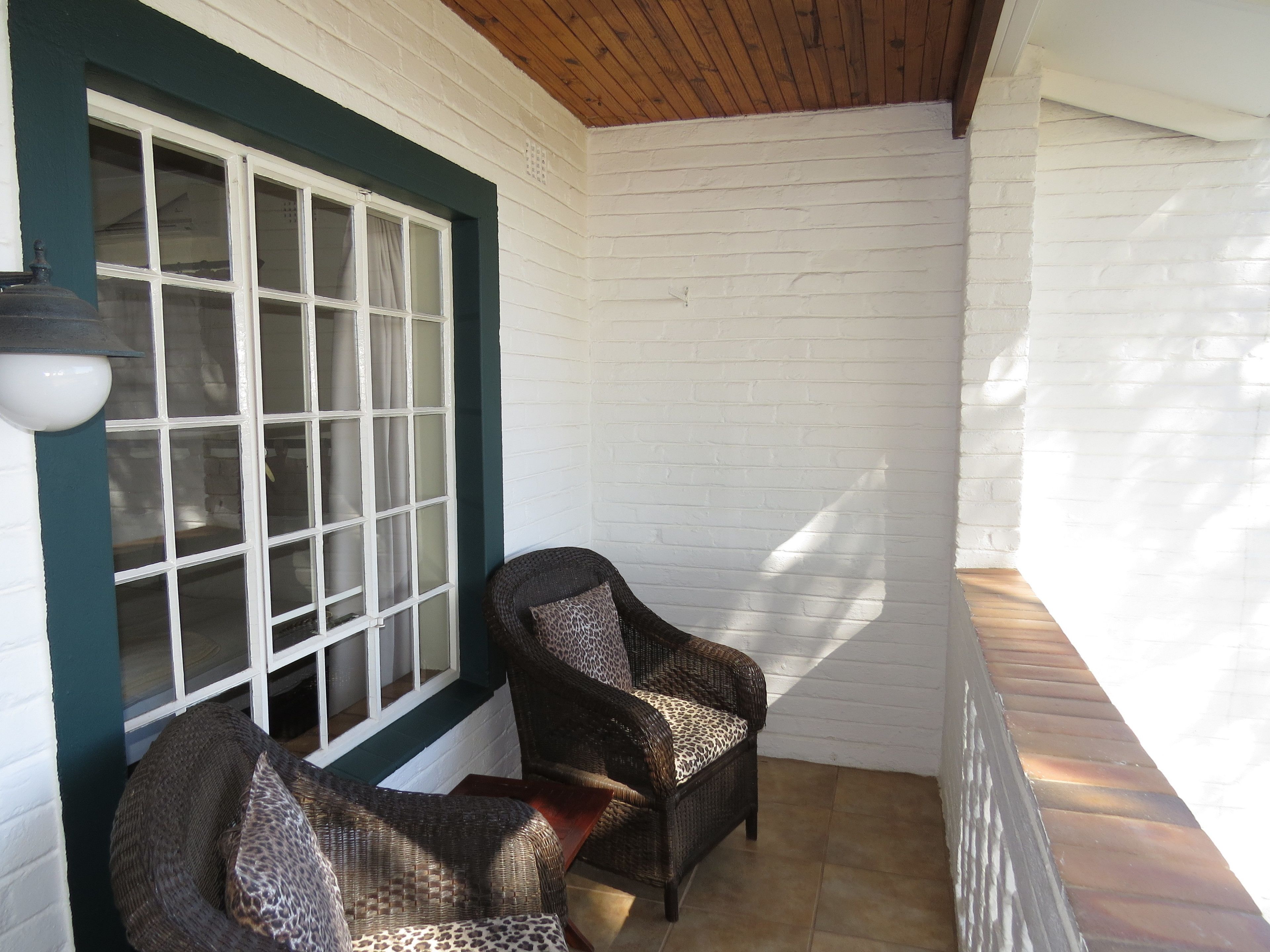 A covered porch with two wicker chairs and a window with curtains.