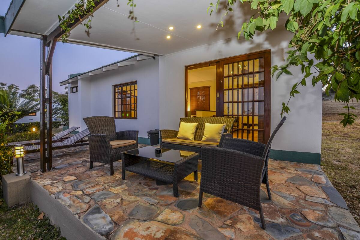 A covered outdoor seating area with wicker furniture, a stone floor, and a view of a traditional building with a sliding door.