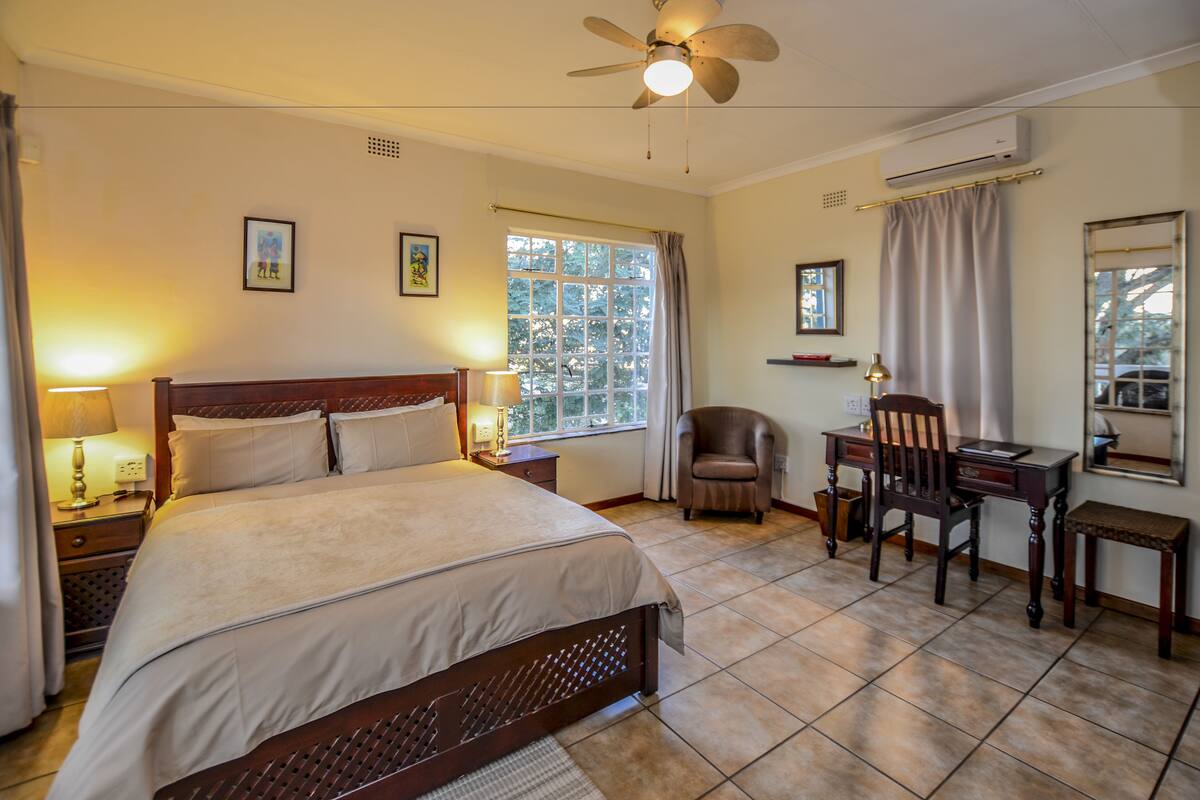 A hotel room with a bed, desk, chair, and large window.