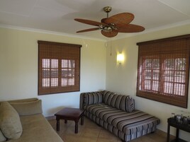 Uma sala de estar com sofá, mesa pequena e ventoinha no teto.