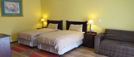 A hotel room with two beds, a sofa, a ceiling fan, and a painting on the wall.