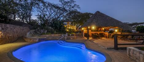 A swimming pool with a thatched-roof structure and outdoor seating area.