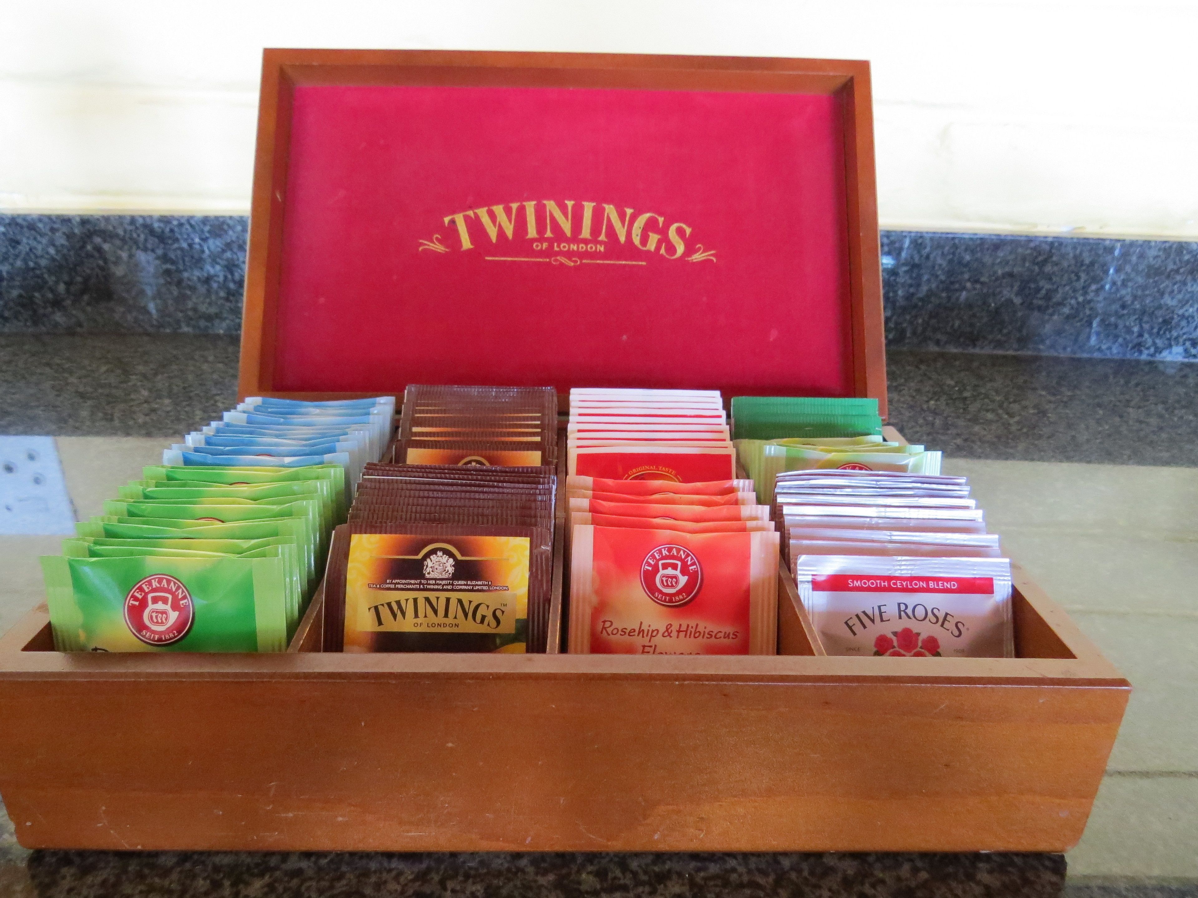 Una caja de madera con compartimentos que contienen varias bolsitas de té etiquetadas como 'Twinings of London'.