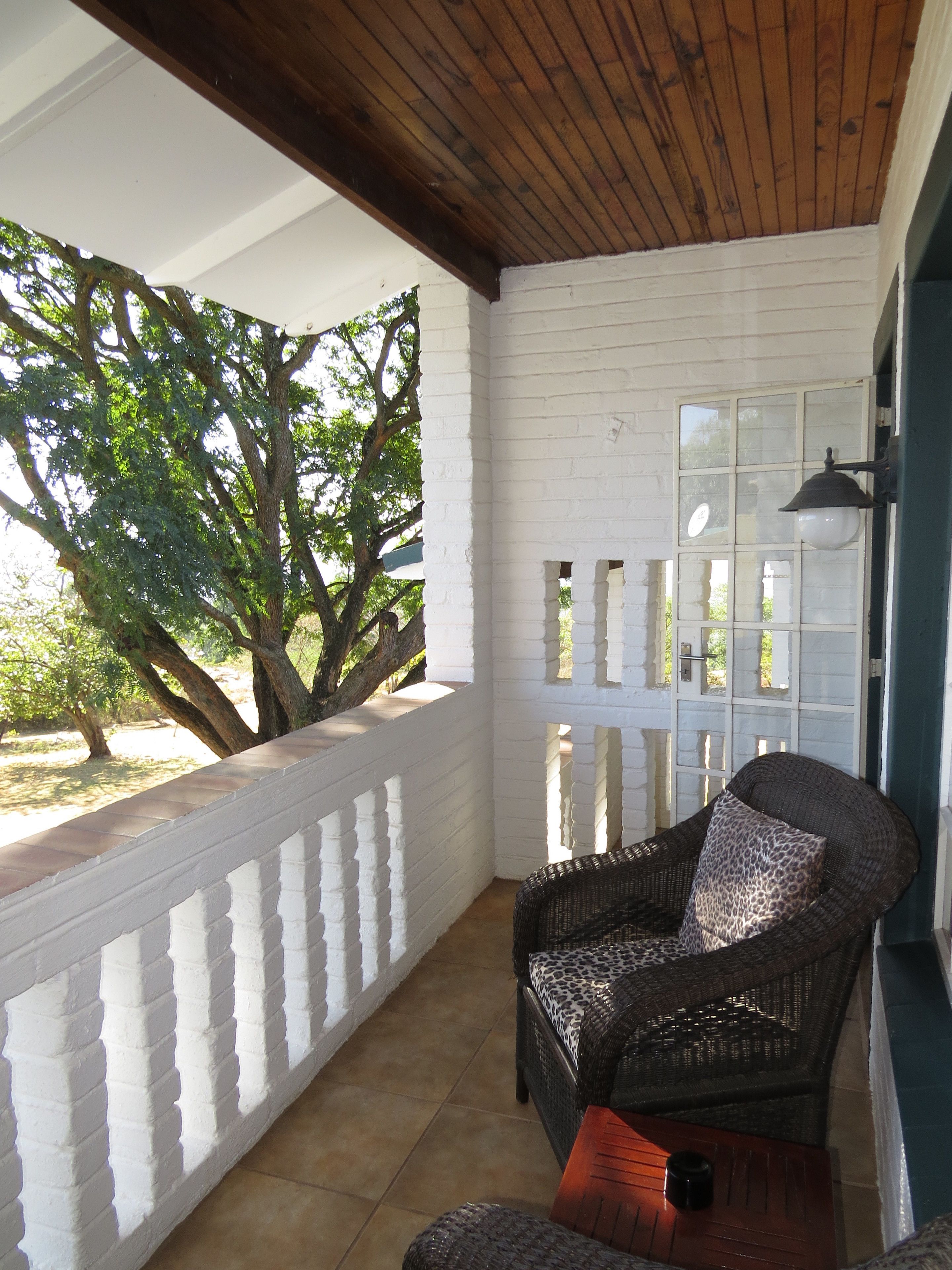 A covered outdoor seating area with a wicker chair and a table, white brick walls, and a wooden ceiling.