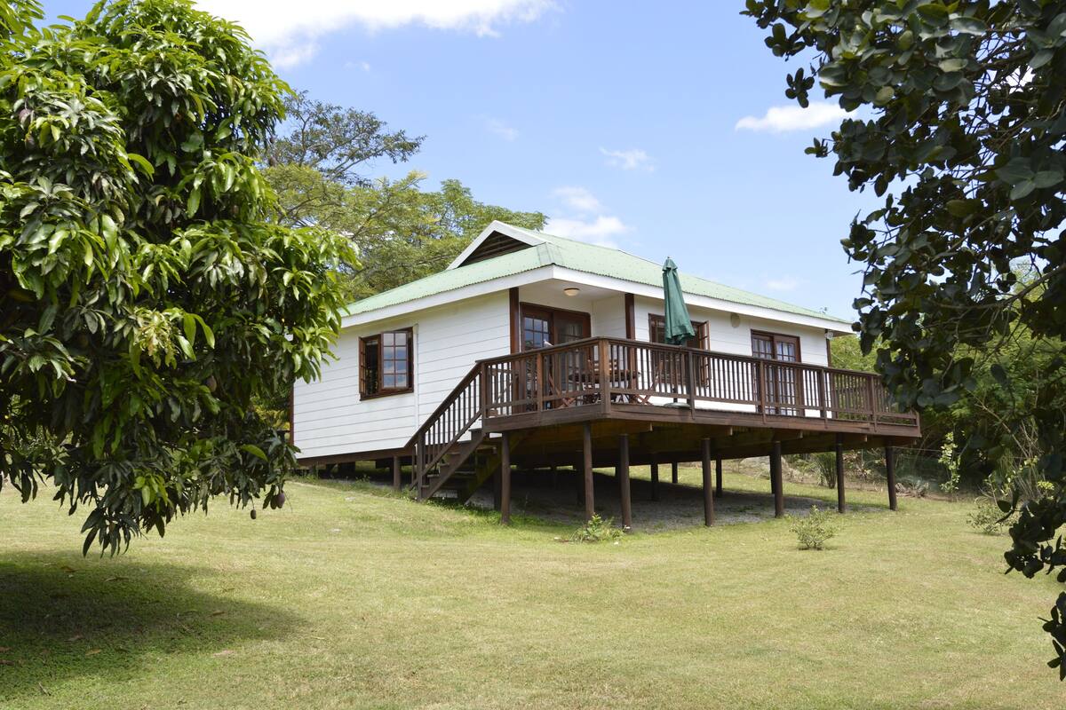 A white house with a green roof, a wooden deck, and a staircase leading to a balcony.