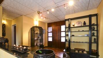 A reception area with a reception desk, a wall-mounted shelf with decorative items, a large mirror, and a door with a wooden frame.