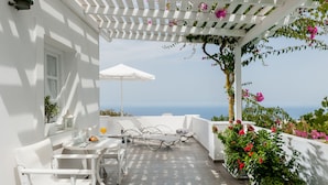 Un patio exterior blanco con mobiliario blanco, una pérgola con flores y vistas al mar.