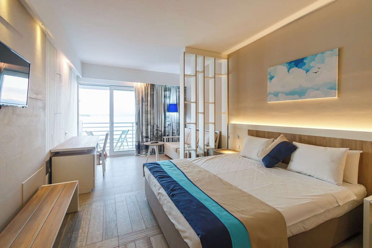 A modern hotel room with a large bed, a desk, and a balcony with a view.