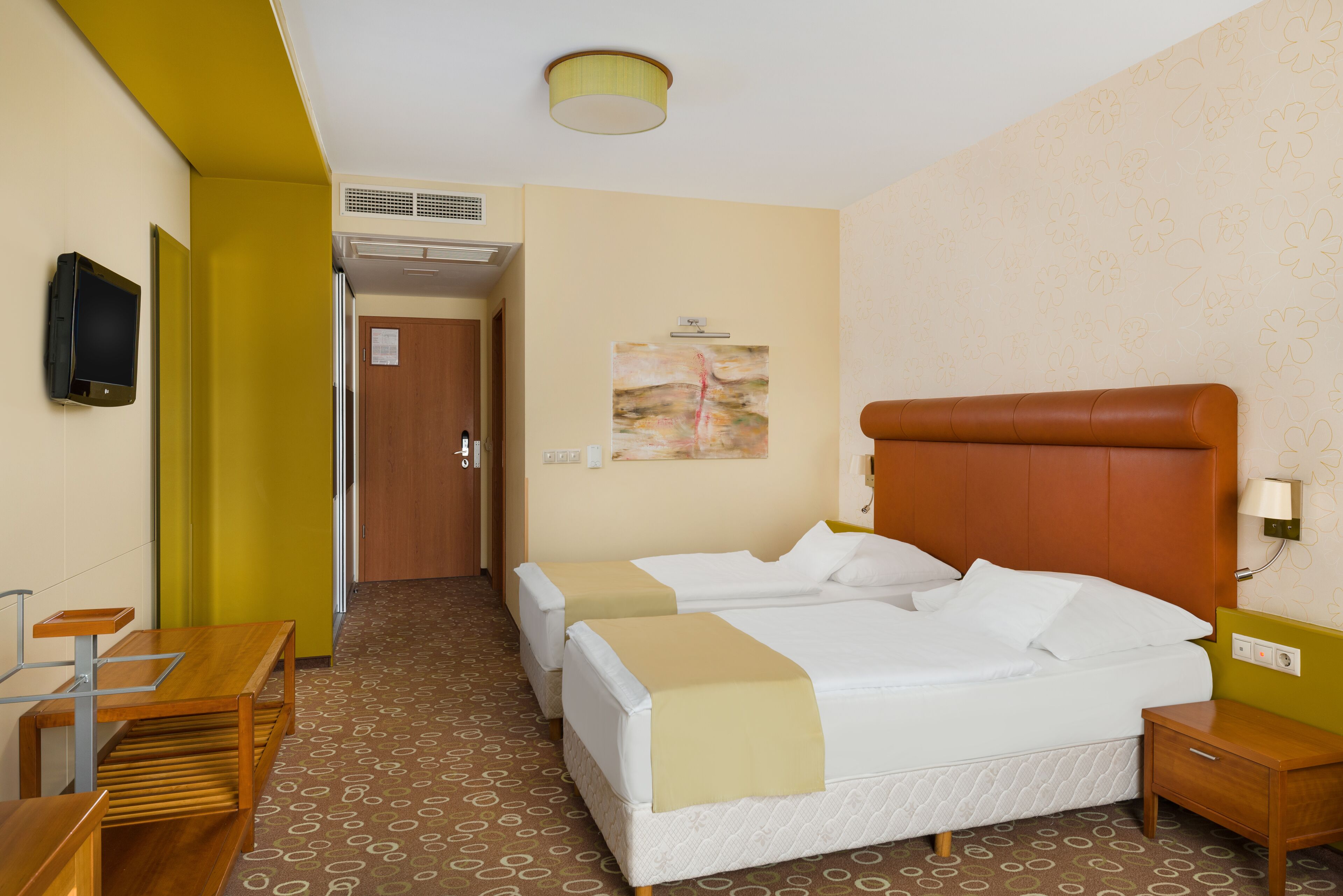 A hotel room with two beds, a wooden desk, a television, and a painting on the wall.