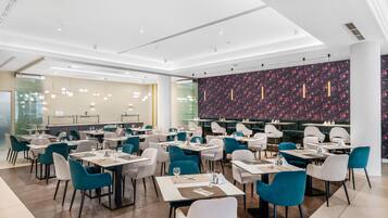 Uma sala de jantar moderna com várias mesas e cadeiras, um espaço de bar com parede estampada e um teto claro com iluminação embutida.