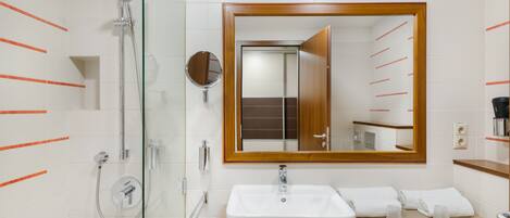 Un baño moderno con ducha envuelta en vidrio, un espejo grande y un mueble de tocador de madera con lavabo.
