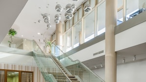 Un interior moderno con una escalera de vidrio, ventanas amplias y lámparas esféricas colgantes.