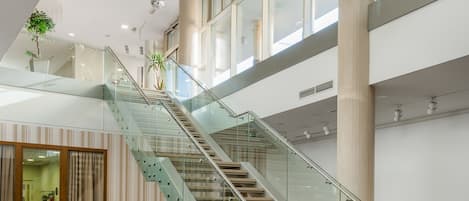 Un interior moderno con una escalera de vidrio, ventanas amplias y lámparas esféricas colgantes.