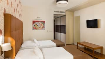 Ein Hotelzimmer mit zwei Betten, einem Fernseher, einer hölzernen Bank und einem Bild an der Wand.