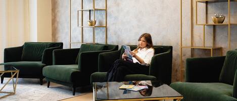 A modern living room with green sofas, a glass coffee table, and gold-framed shelves.