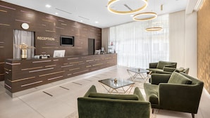 Zona de recepción de diseño moderno, con mostrador de recepción, televisor de pantalla plana y área de descanso con sillas tapizadas en verde y una mesa de centro de vidrio.