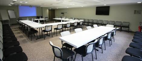 A conference room with multiple tables and chairs, a projector screen, and a whiteboard.