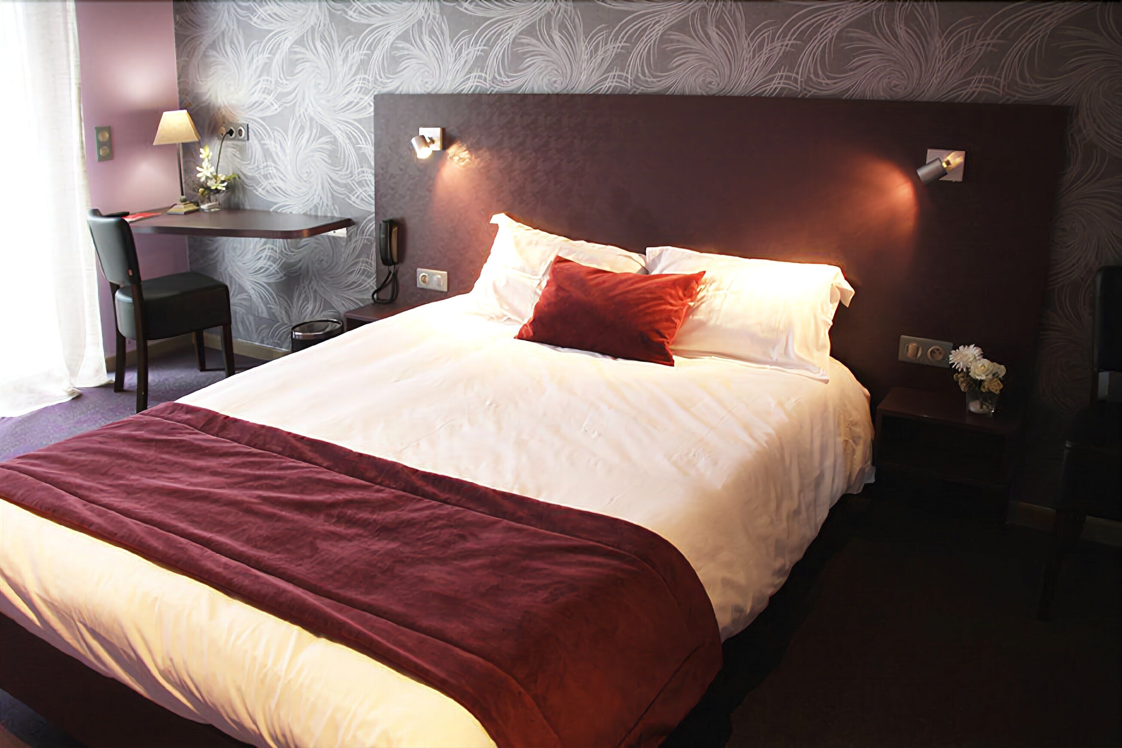 Ein Hotelzimmer mit einem großen Bett, einem Schreibtisch mit Stuhl und einem Nachttisch mit Lampe.