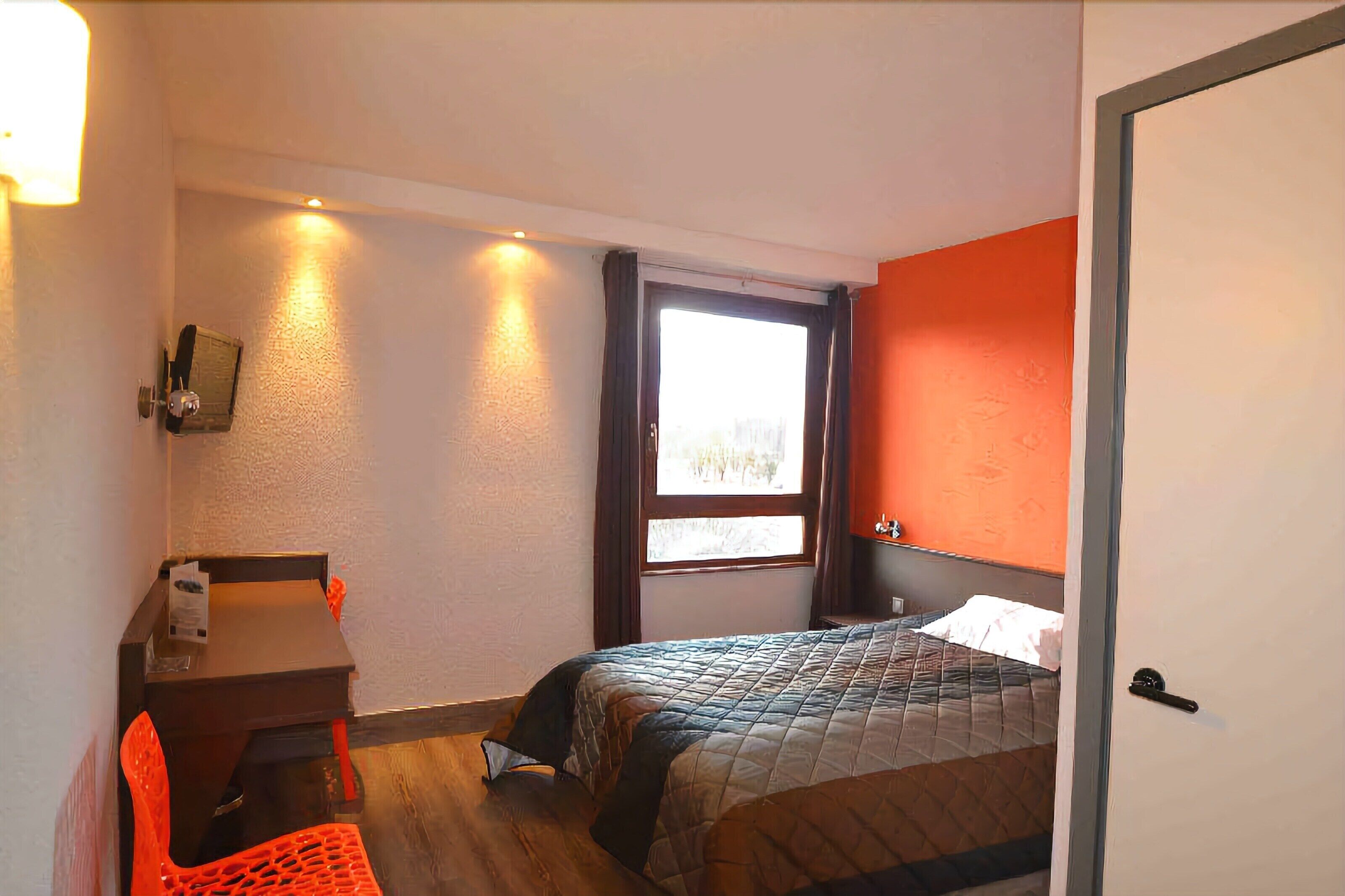 Una habitación de hotel pequeña con una cama, un escritorio con una silla, una ventana y una puerta.