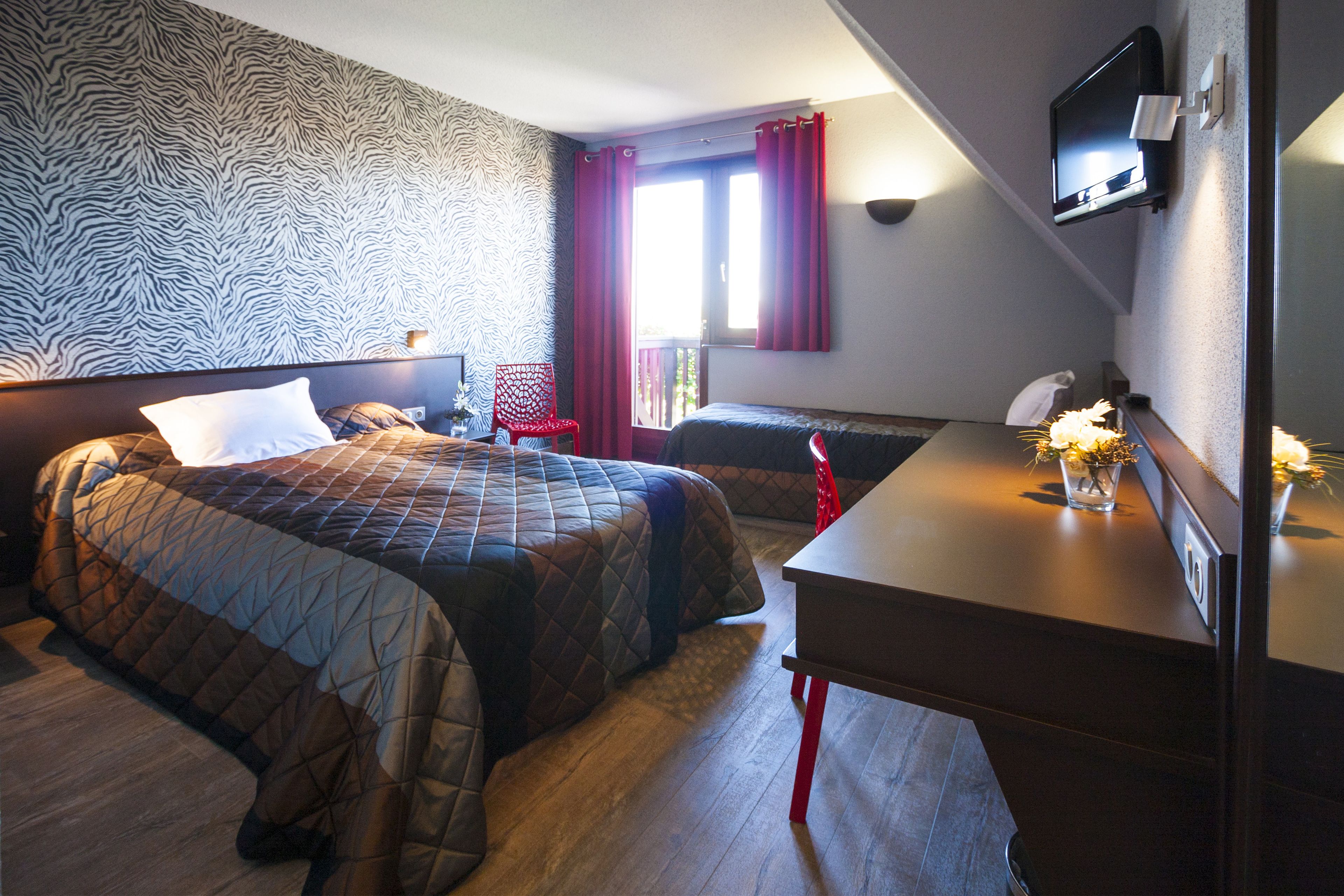 A hotel room with two beds, a desk, a TV, and a window with curtains.