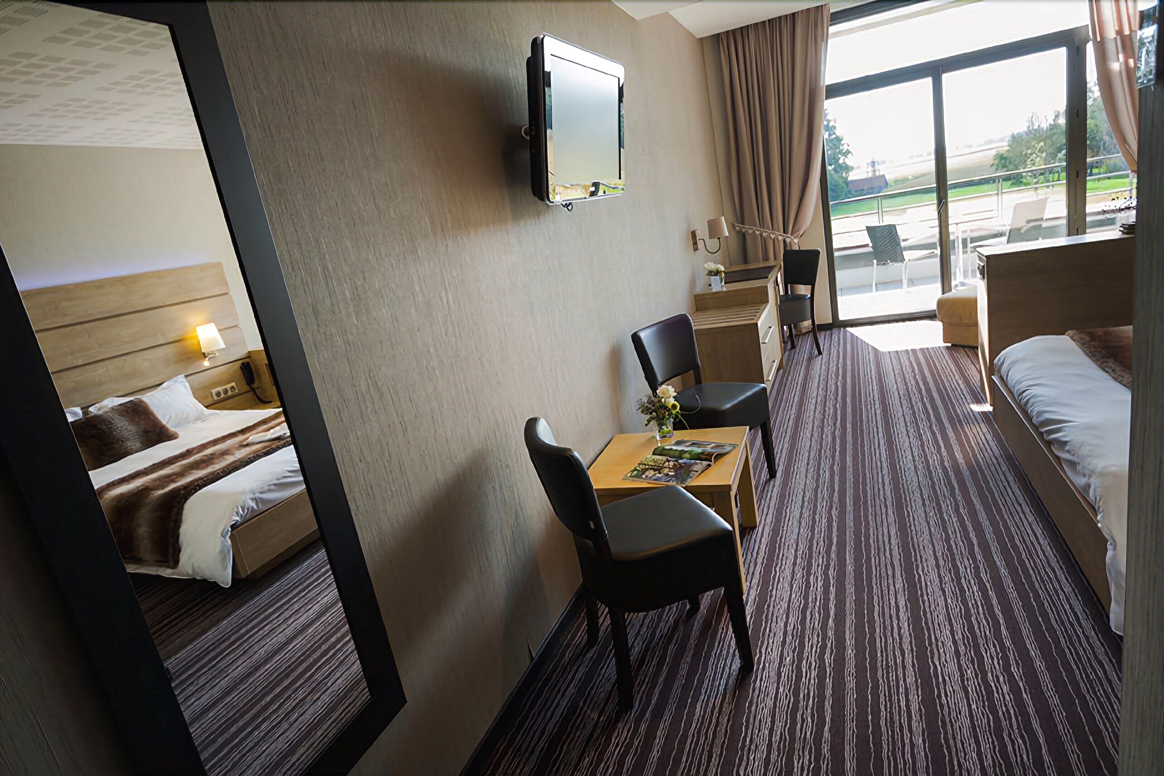 Habitación de hotel con cama, escritorio, silla, televisor y vistas al exterior.