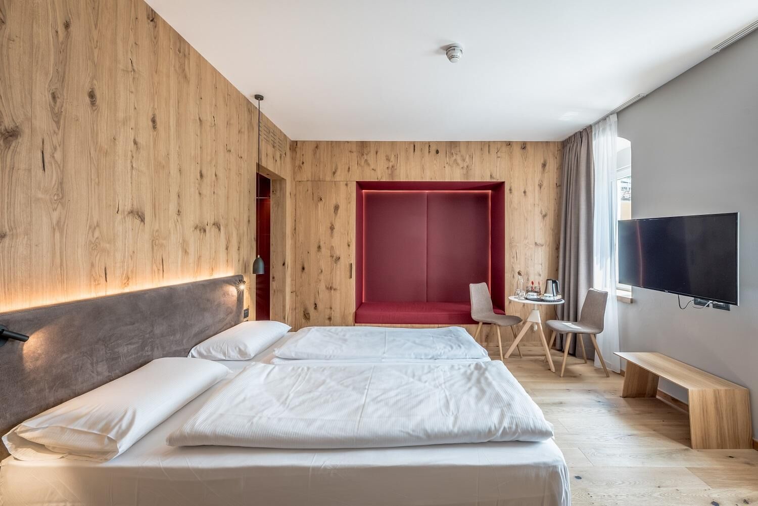 Una habitación de hotel moderna con una cama grande, una zona de estar roja, un escritorio con una silla y un televisor montado en la pared.