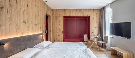 Una habitación de hotel moderna con una cama grande, una zona de estar roja, un escritorio con una silla y un televisor montado en la pared.