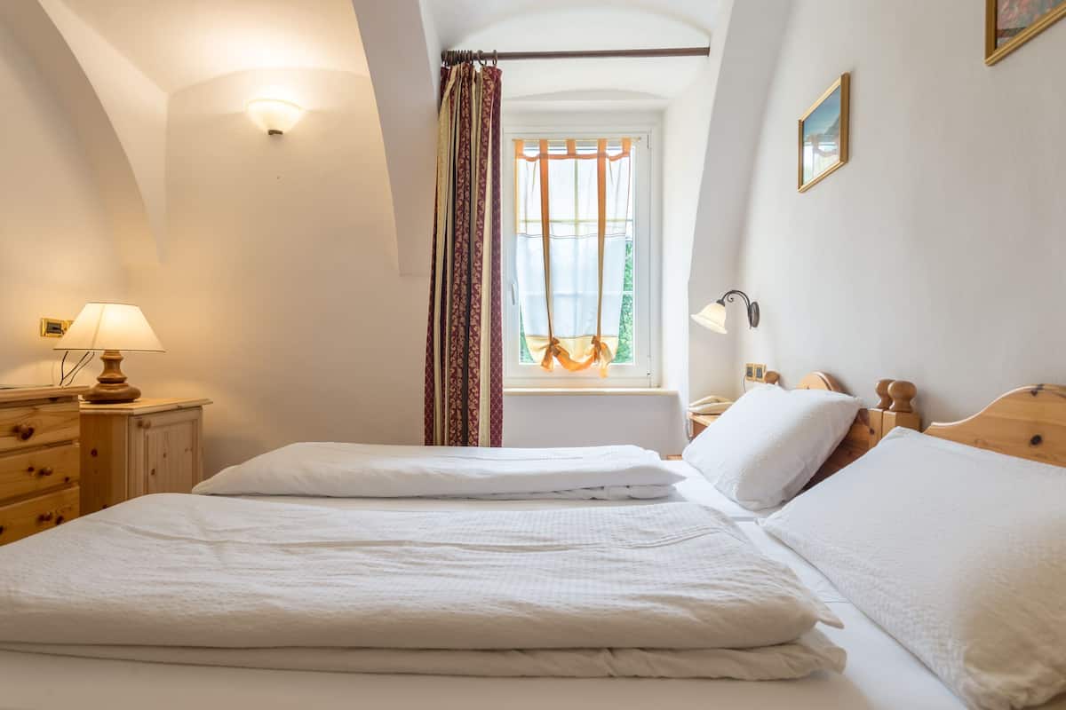 A bedroom with a bed, bedside tables, a lamp, a window with curtains, and a wall-mounted light fixture.