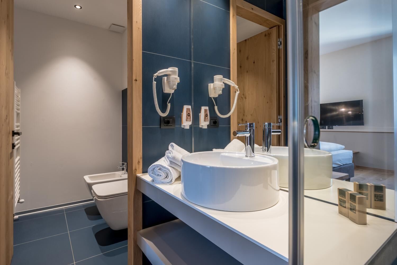 A modern bathroom with a large mirror, two sinks, a toilet, and a shower.
